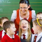 Teacher with students in school uniforms in front of green chalkboard